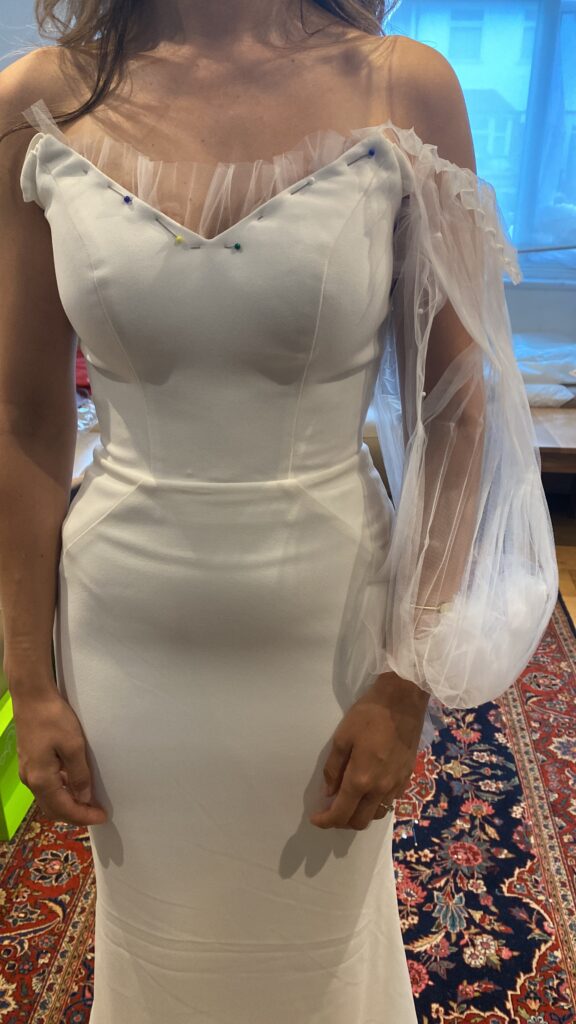 Pinned illusion neckline fitting during bespoke bridal sleeve reconstruction on a minimalist wedding dress