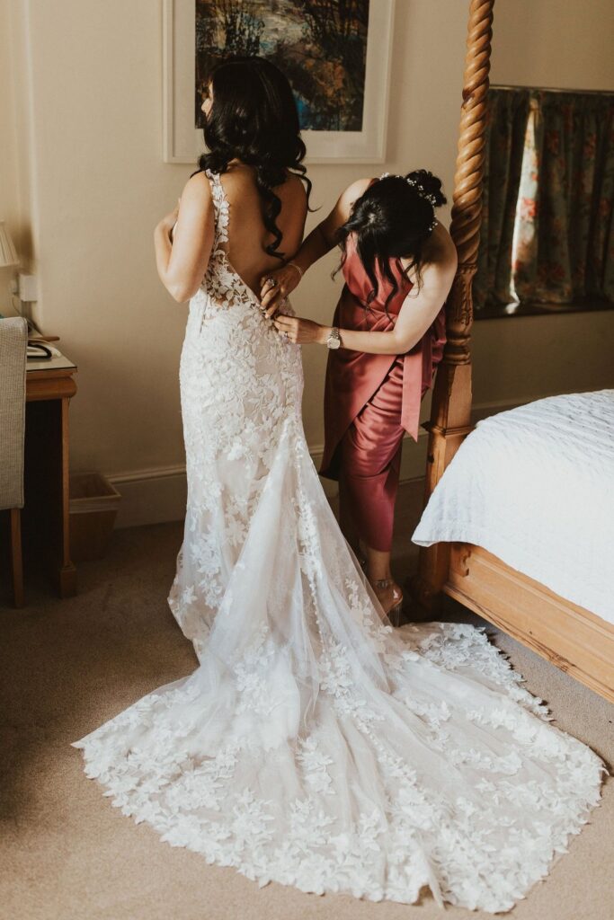 Allure Bridal alterations – bride getting ready in her perfectly fitted Allure Bridal wedding dress bridesmaid closing buttons 