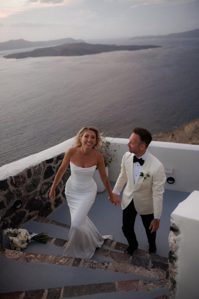 Bride and groom walking through the streets of Santorini with the bride wearing a beautifully fitted Khya wedding dress