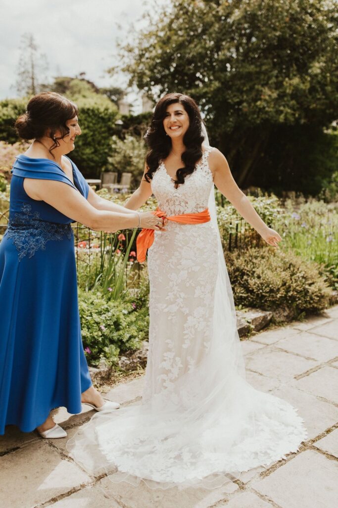 Allure Bridal alterations – bride getting ready in her perfectly fitted Allure Bridal wedding dress mother tieing Sash