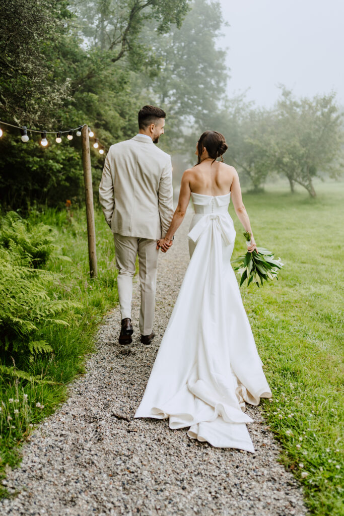 Bride and groom walking together showing fitted mikado wedding dress with bow back detail after bridal alterations Horsham