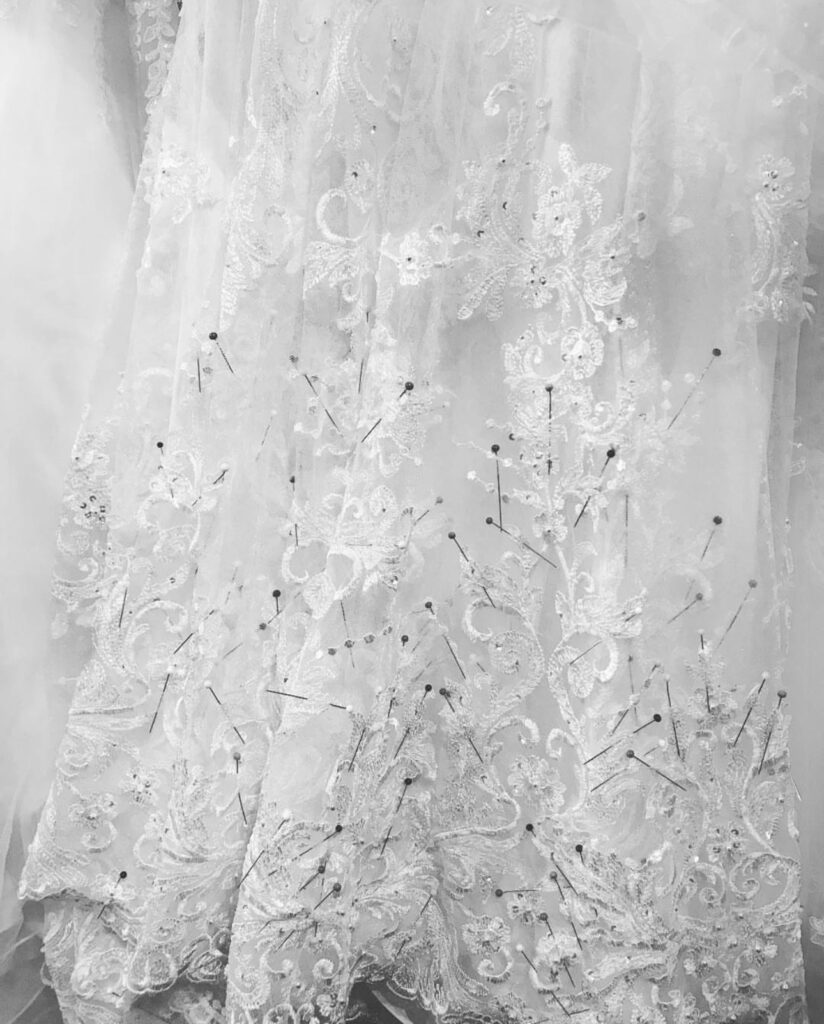 Close-up of a Galia Lahav couture wedding dress hem during alterations showing lace scallops, internal pinning and hem reshaping work.