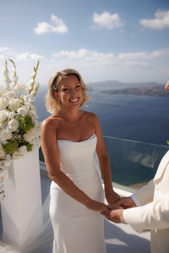 Bride and groom exchanging vows in Santorini with the bride wearing a professionally altered Khya Studios wedding dress.