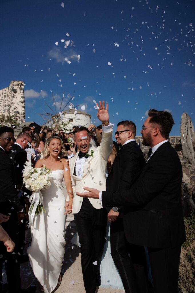 Bride and groom confetti celebrations in Santorini with the bride wearing a professionally altered Khya Studios wedding dress.