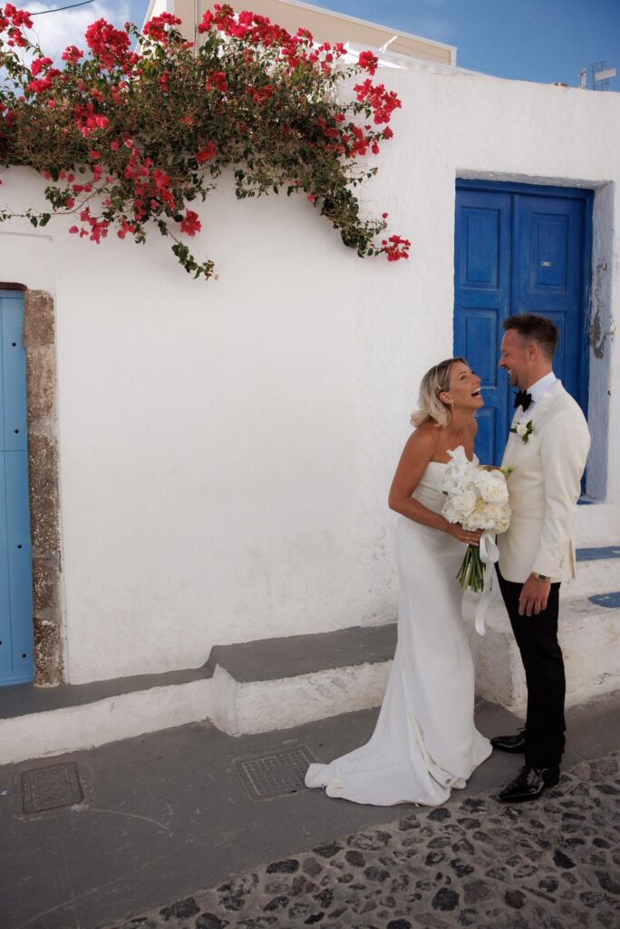 Bride and groom walking through the streets of Santorini with the bride wearing a beautifully fitted Khya wedding dress
