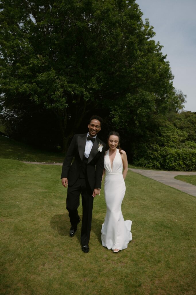 Bride and groom after Made With Love bridal alterations with the Audrey wedding gown perfectly fitted outside holding hands 