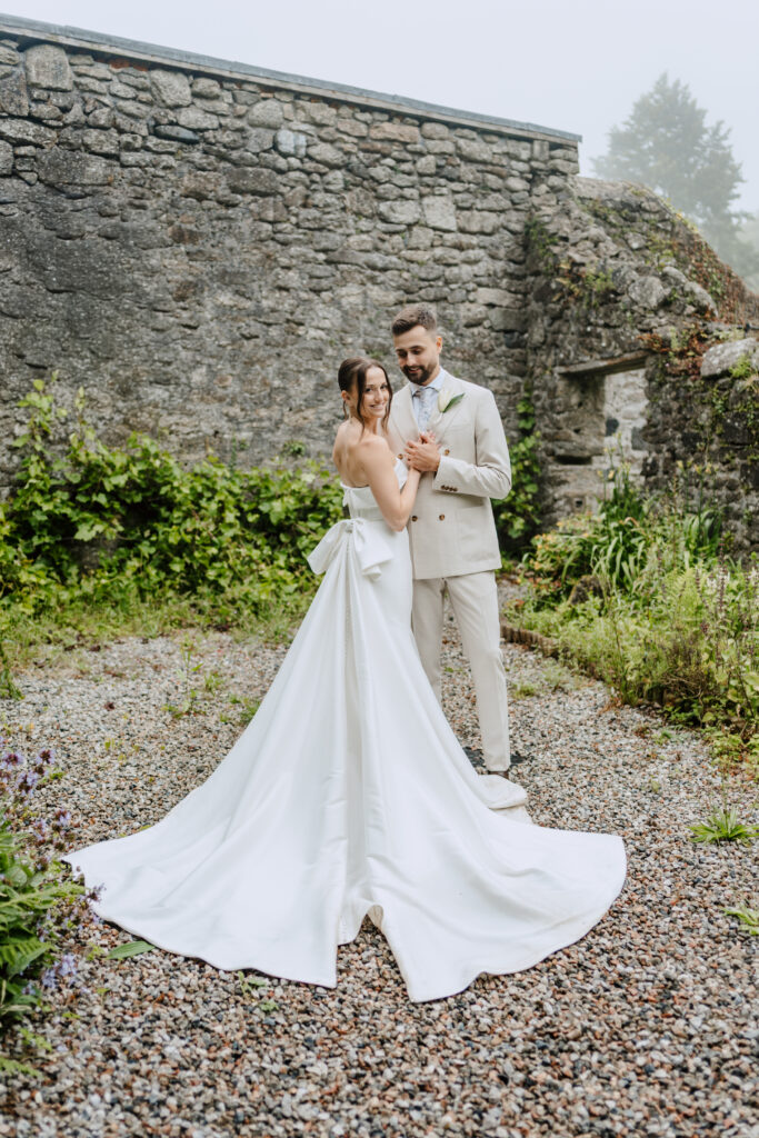 Bride and groom walking together showing fitted mikado wedding dress with bow back detail after bridal alterations Horsham