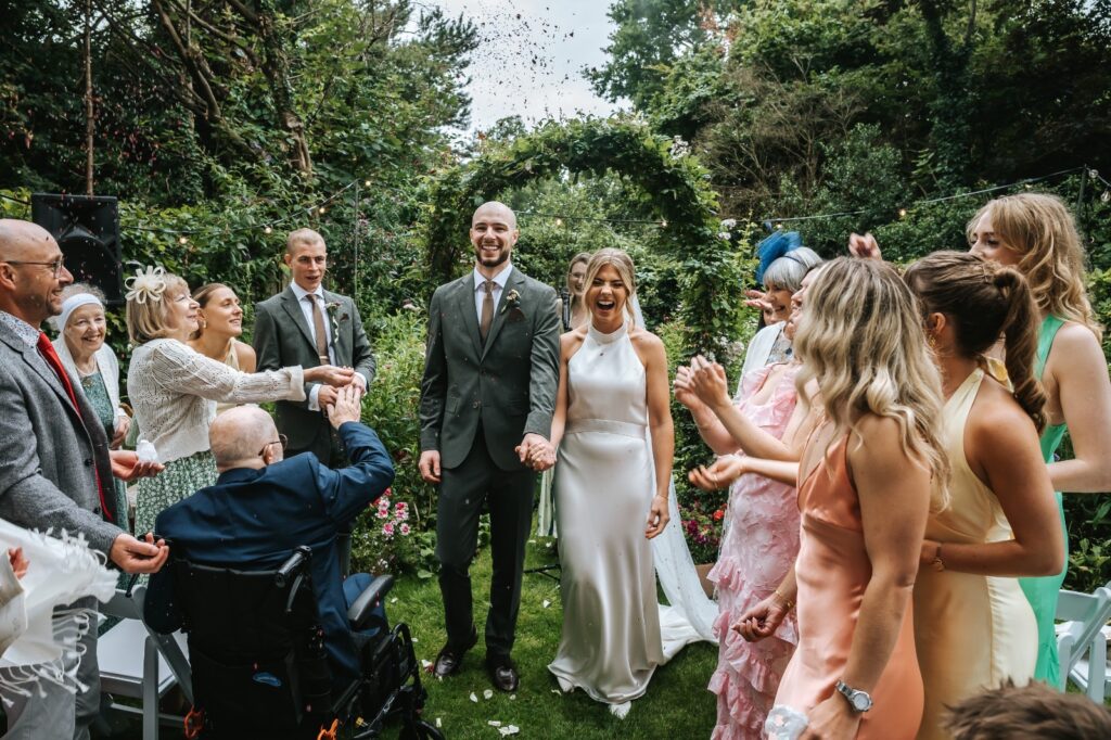 Redhill bride wearing a Catherine Deane Kin gown after couture bridal alterations, posing with her groom after the ceremony confetti celebration.