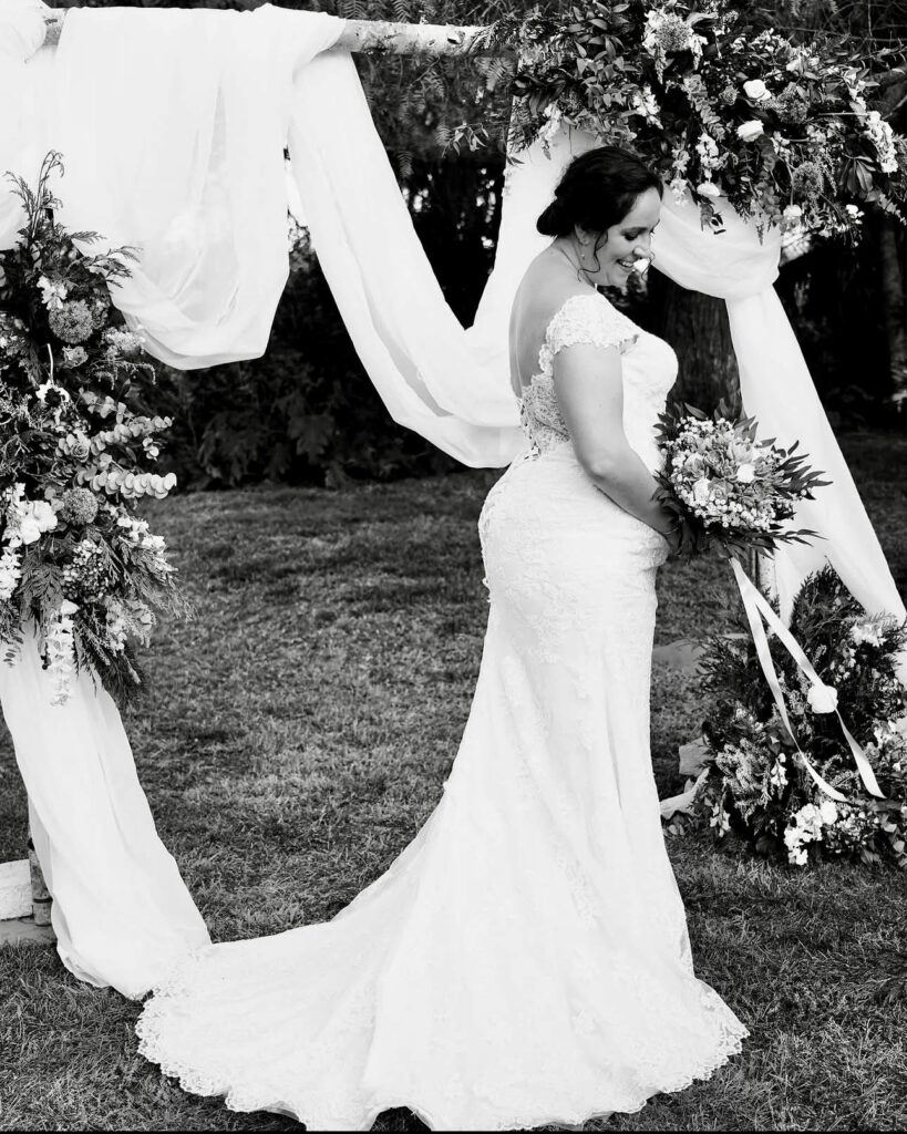 Wedding Dress Alterations Morden bride Sarah wearing her altered lace wedding dress beneath a floral ceremony arch
