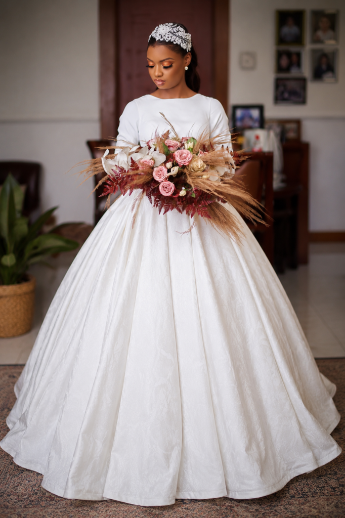 Lagos International bride wearing a timeless long sleeve satin wedding dress altered in Sutton, with a full ballgown skirt and statement bouquet.