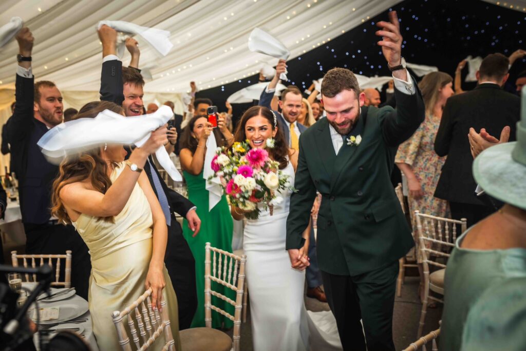 bride and groom entering reception area after wedding with celebrating guests.