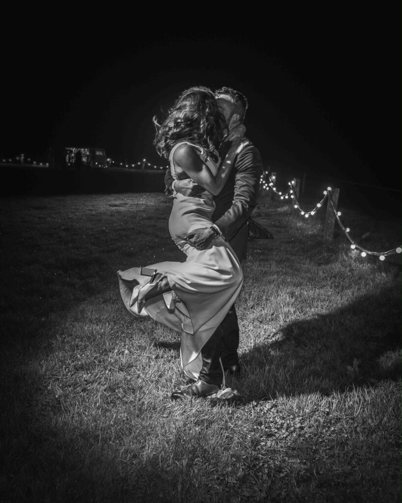 Groom liftinh bride during dancing on wedding day outside at night.