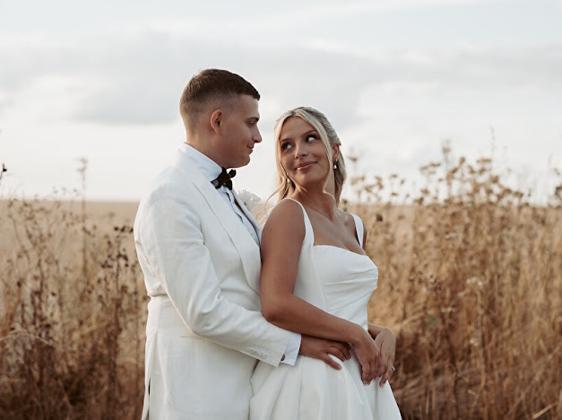 Bride and groom embracing beside a field in their wedding outfits