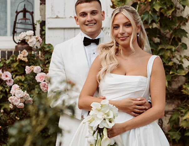 Black-and-white portrait of the bride in her Ermana gown beside a man wearing a black tuxedo