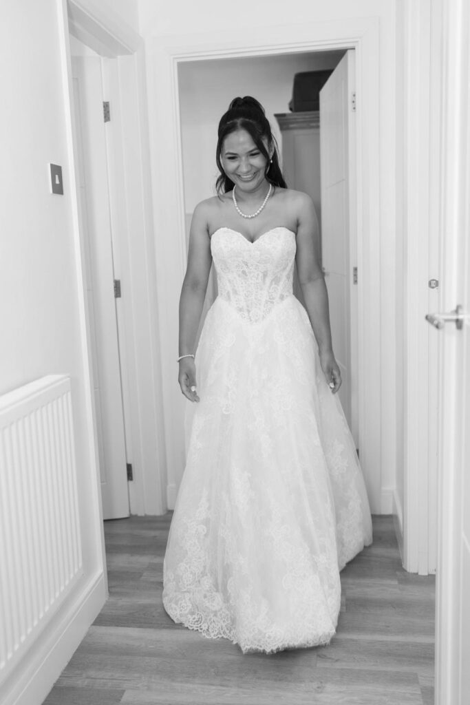 Black-and-white full-length portrait of the bride in her altered Anna Sorrano Mercia wedding dress standing in a doorway