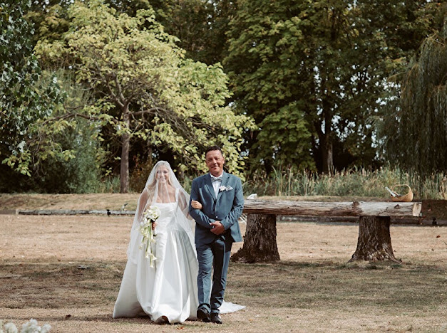 Bride wearing her veil over her face and walking arm in arm with her escort outdoors