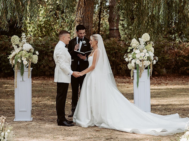 Bride and groom holding hands during their outdoor ceremony, with her train and veil extended