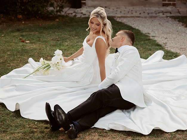 Bride and groom seated on a lawn with the Mikado skirt and buttoned train spread around them Milla Nova Ermana wedding dress alterations.