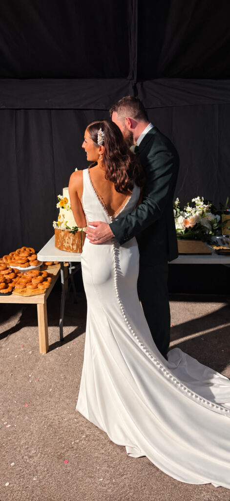 Raynes Park Bride wearing her stunning Essense of Australia dress cutting the cake with groom back view train.
