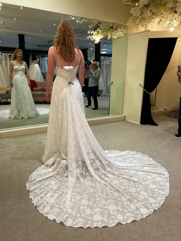 Back view of bride wearing Stella York 8055 with its floral train spread out in a bridal boutique showing how big it was on her before alterations.