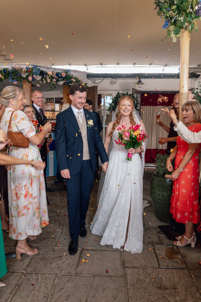 Bride in her altered Stella York 8055 dress walking with the groom beneath falling confetti Worcester Park Bridal Alterations.
