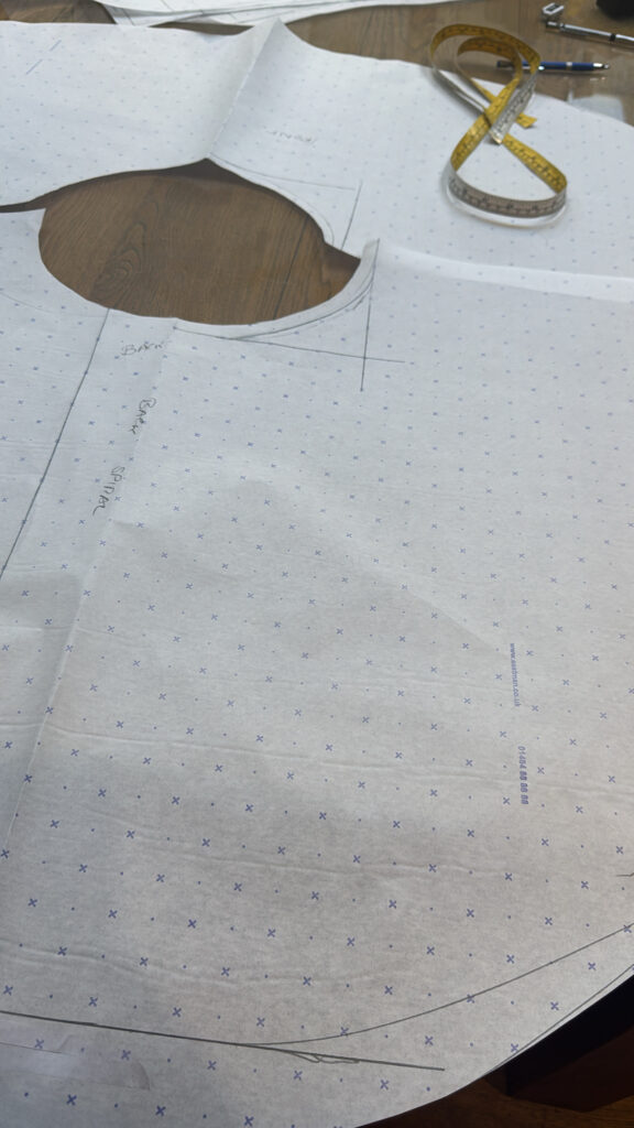 Hand-drafted fitted dress pattern with asymmetric circle skirt pieces positioned over traditional wax-print fabric.