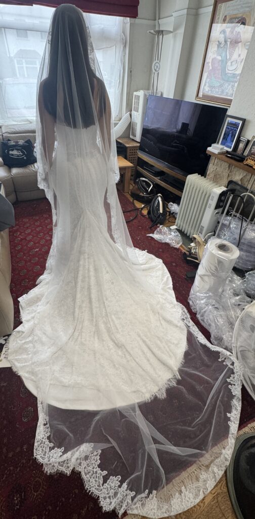 Bride wearing the WONA Concept Bronx lace wedding dress during alterations, showing the back view of the structured corset bodice, fitted silhouette and cathedral veil for this Cobham Bridal Alterations.