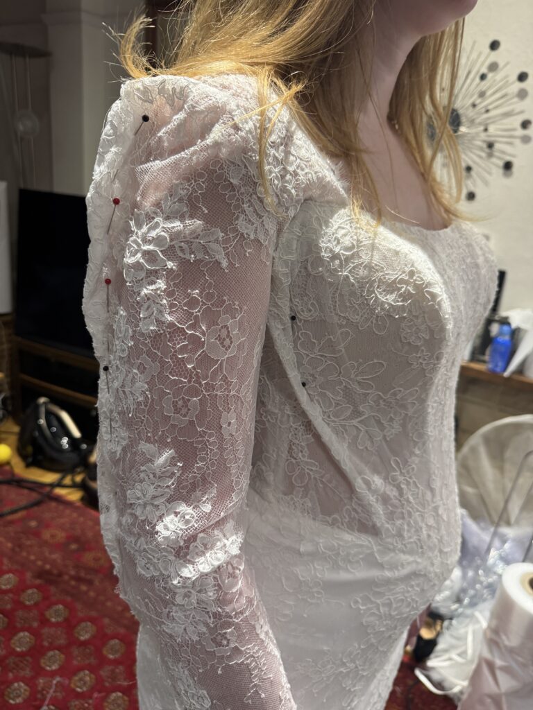 Maggie Sottero Ariadne lace sleeve and shoulder alterations showing precise pinning during bridal fitting in Sutton