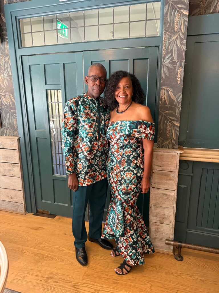 Mother of the bride modelling her finished bespoke teal and rust wax-print dress made from scratch with pattern drafting to final at the Party in Cheltenham with her husband in matching Wax print Shirt.