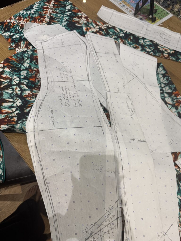 Hand-drafted fitted dress pattern pieces positioned over traditional wax-print fabric.