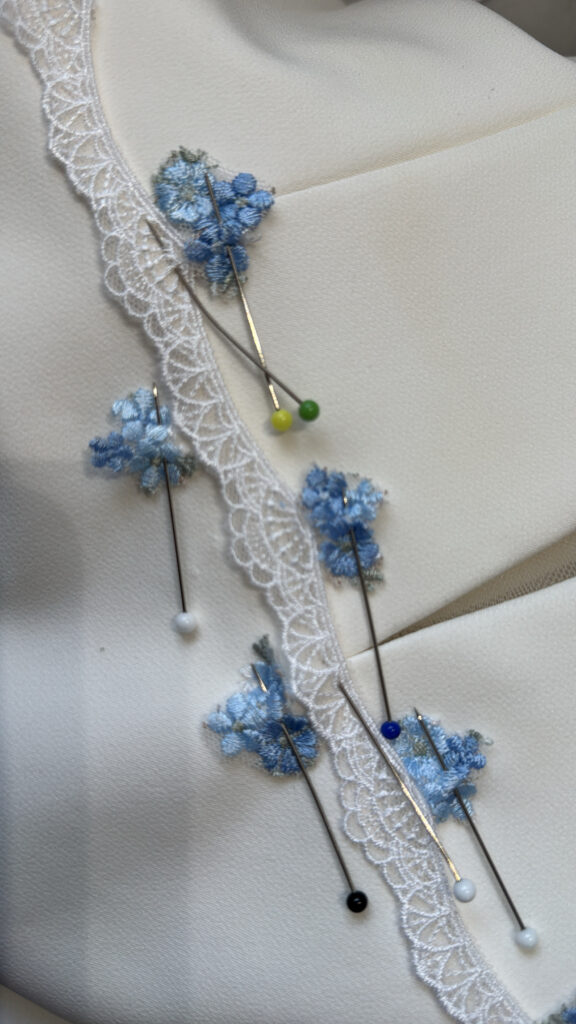Individual blue embroidered floral appliqués being positioned on Madi Lane wedding dress