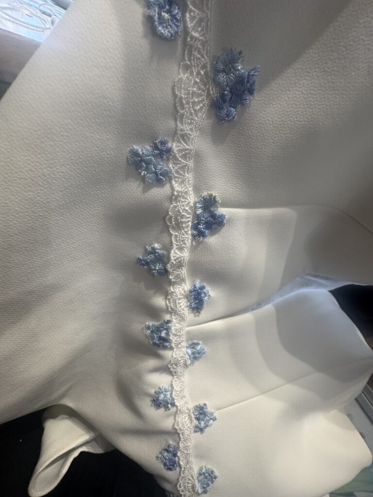 Individual blue embroidered floral appliqués being positioned on Madi Lane wedding dress hand stitched one at a time.