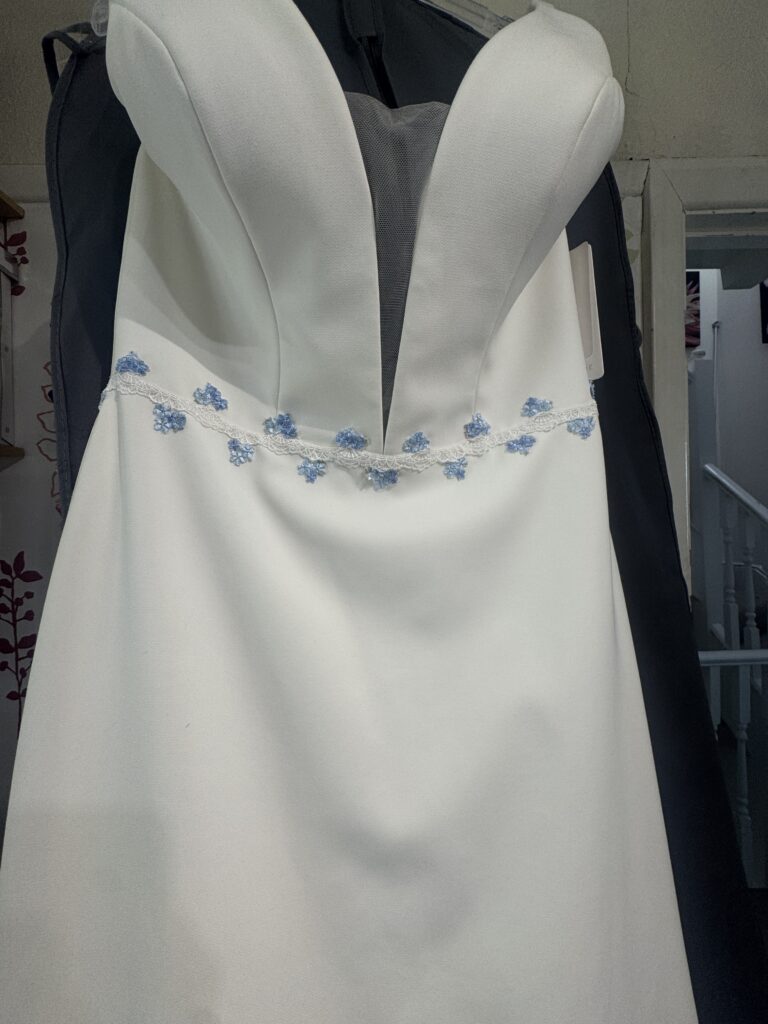 Hand sewn blue floral motifs and white lace positioned around wedding dress waist