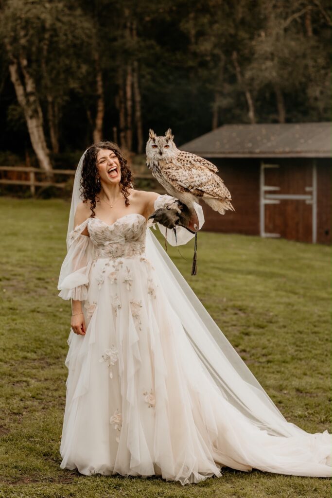 Mia laughing while holding an owl in her floral embroidered Morilee wedding dress with flowing veil