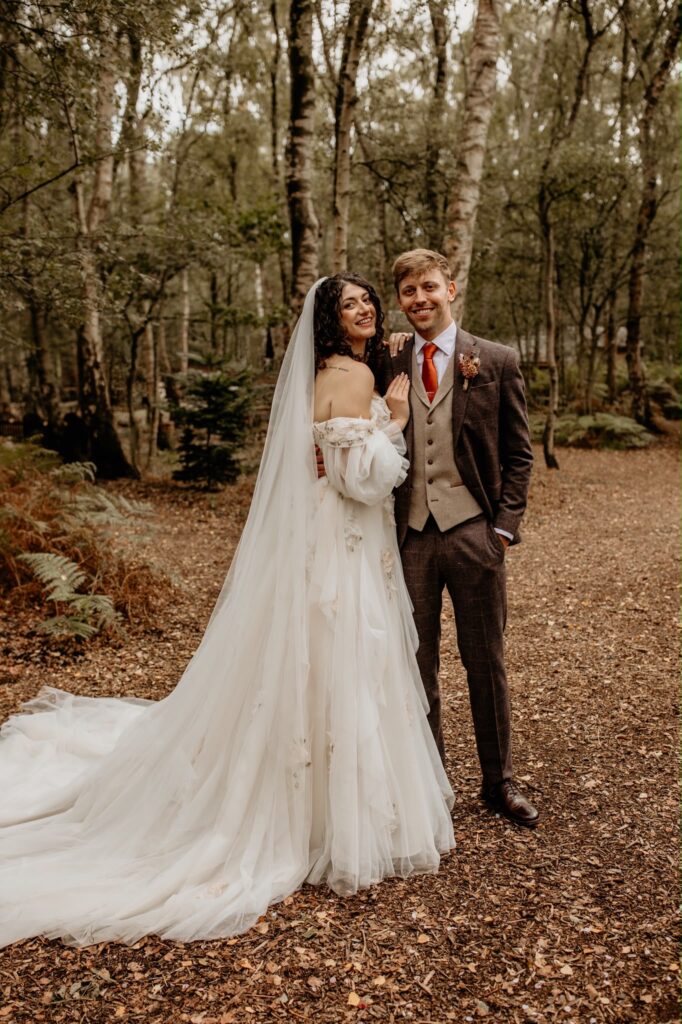 Raynes Park Morilee bridal alterations showing Mia in her beautifully fitted floral wedding gown with flowing tulle train in the woodlands with groom on the wedding day.