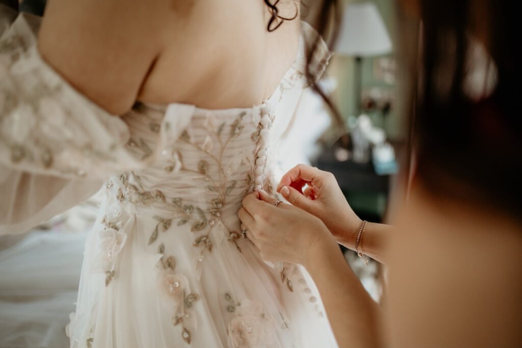 Close-up of fabric-covered buttons being fastened on Mia's embroidered Morilee wedding dress