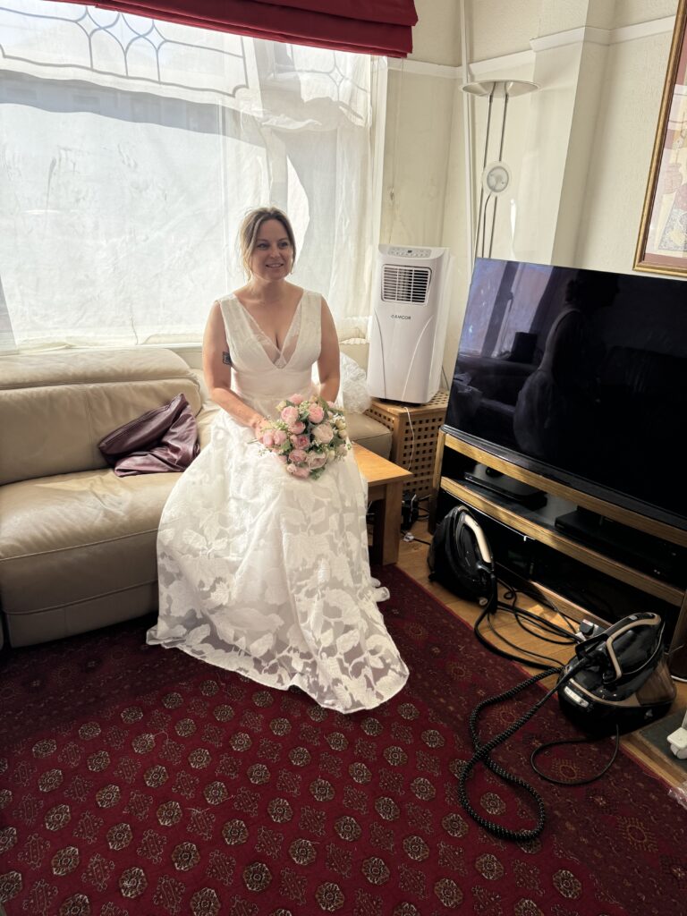 Bride seated with a pink bouquet wearing her floral wedding dress after adjustments in Sutton.