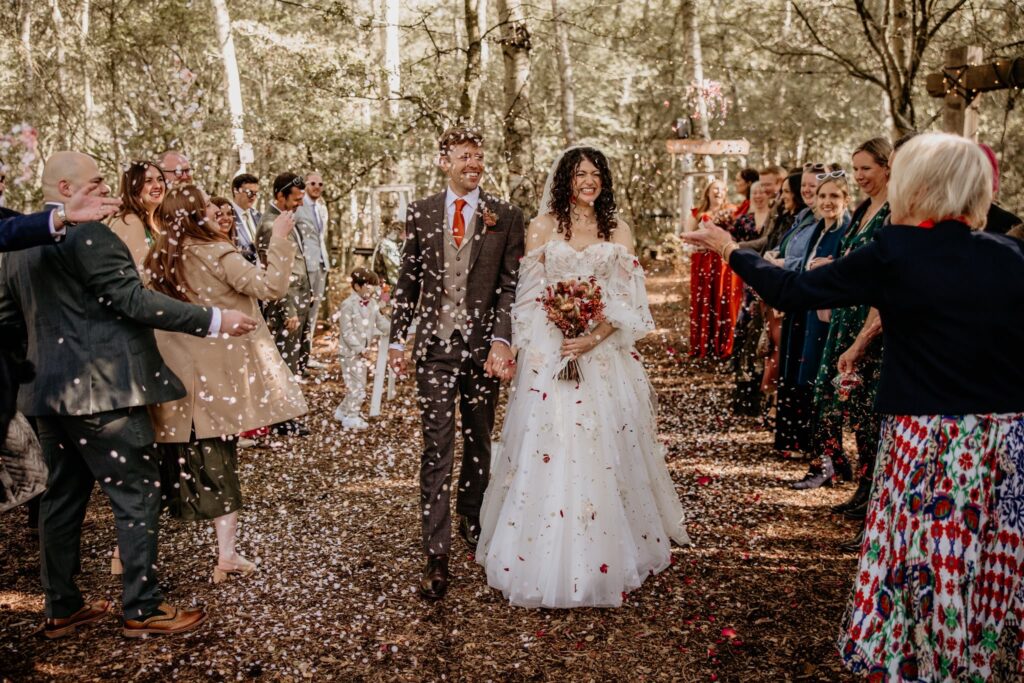 Newlyweds walking through confetti surrounded by guests at their woodland wedding celebration