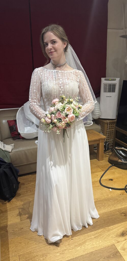 Bride wearing her Heidi Hudson Marisol gown with a veil and bouquet at her fitting with a WED2B bridal alterations expert in Sutton