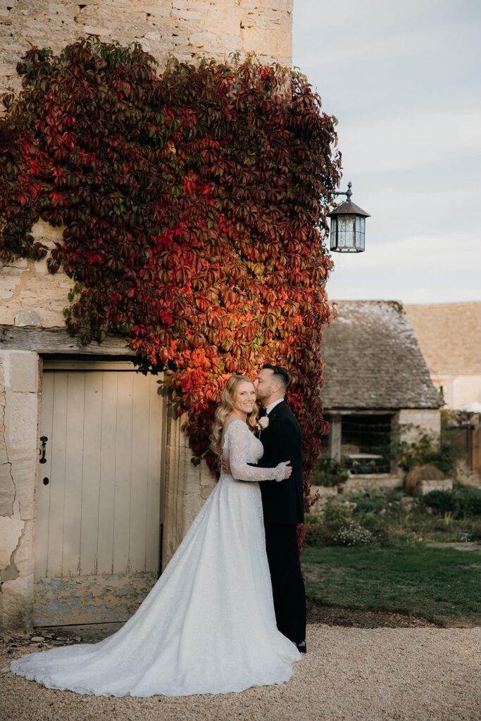 Bride and groom beside autumn foliage with the bride wearing her altered Yedyna Estia lace wedding dress.